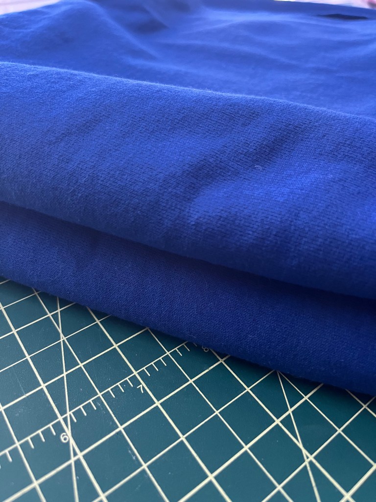 folded blue sweatshirt fleece fabric sitting on a green cutting mat with yellow lines 